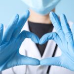 Healthcare worker wearing a mask and gloves making a heart shape with hands.