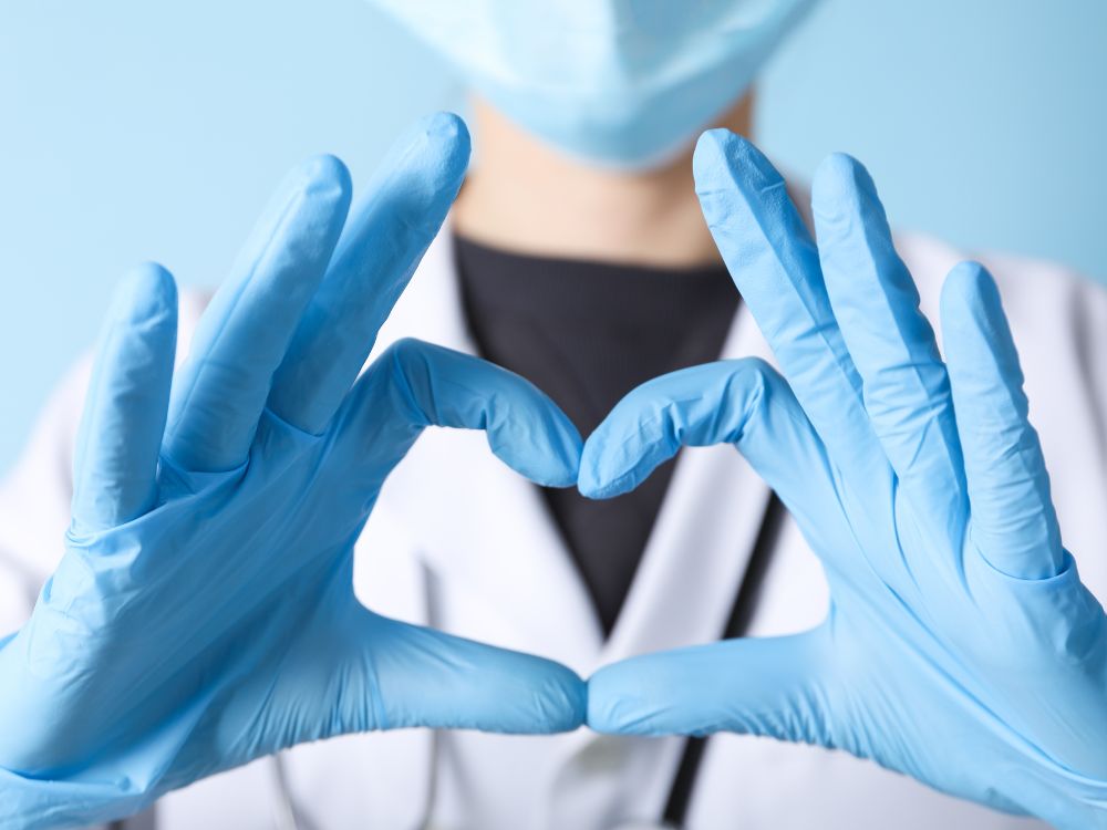 Healthcare worker wearing a mask and gloves making a heart shape with hands.