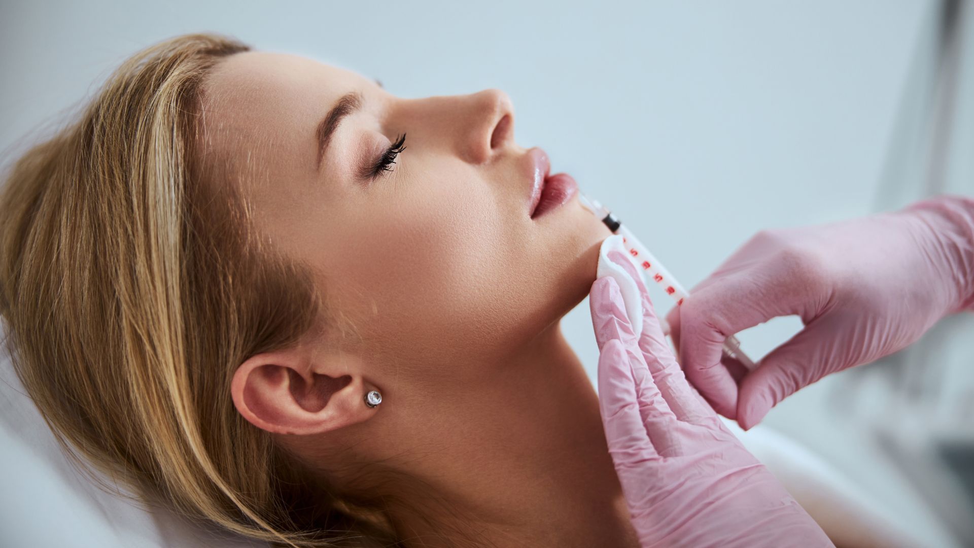 Professional cosmetologist injecting a dermal filler into the patient lips