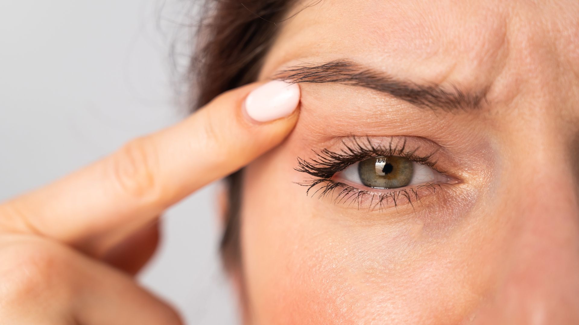 Close-up Portrait of Caucasian Middle-Aged Woman Pointing to the Wrinkles on the Upper Eyelid. Signs of Aging on the Face