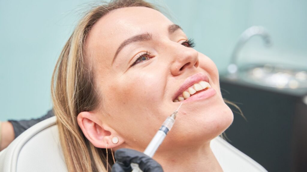 A smiling patient undergoing a dental botox procedure near the lips to enhance aesthetics and correct gummy smiles